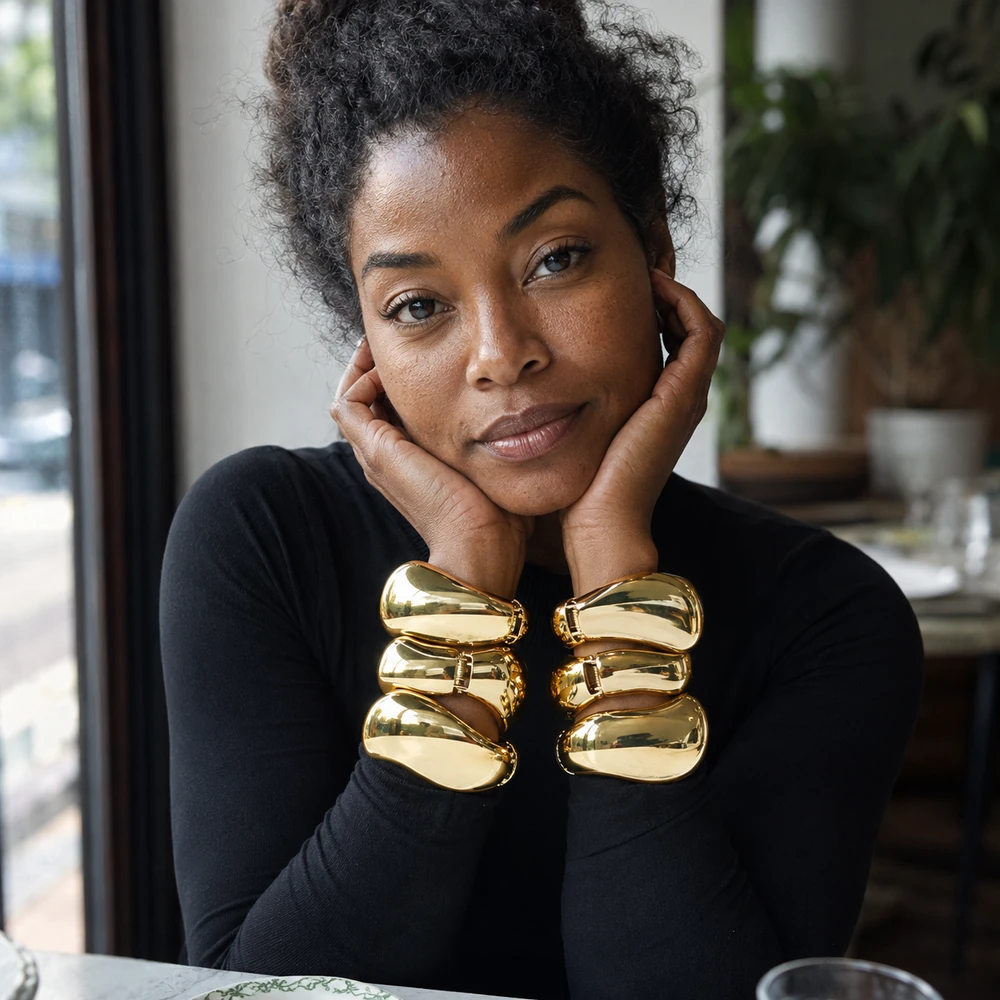 melinda-sculptural-gold-cuff-bracelet-cafe-lifestyle-01 Gold-tone sculptural bangles shown in a layered wrist styling portrait